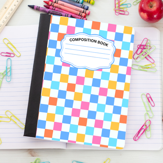 A composition book with a colorful checkered pattern in blue, pink, orange, and yellow, placed on an open lined notebook surrounded by school supplies like paperclips, crayons, and an apple.