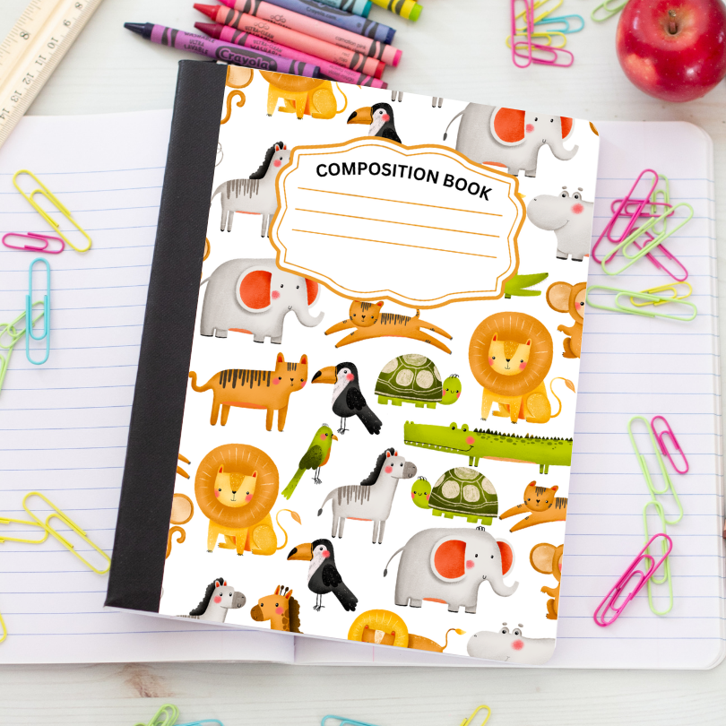 A children's composition notebook with a black spine and a white cover decorated with colorful cartoon animals, shown on a lined desk with paperclips, crayons, and an apple.