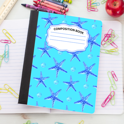 A composition notebook with a bright turquoise cover decorated with blue starfish and pearl-like dots, placed on an open lined notebook surrounded by colorful paperclips, crayons, a ruler, and an apple.