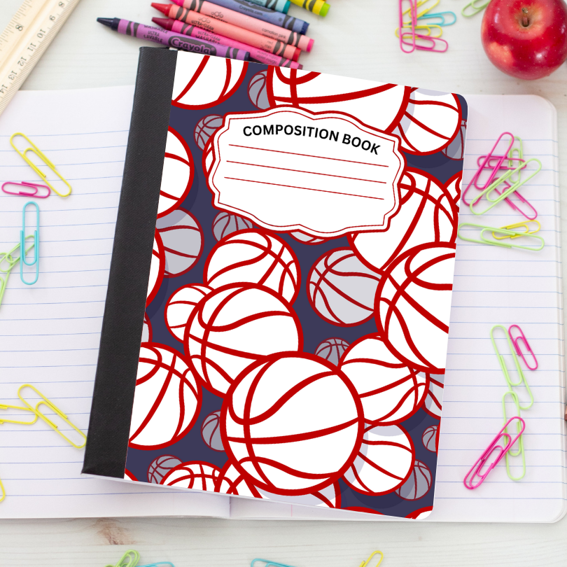 A composition notebook with a basketball pattern cover, placed on a lined notebook page surrounded by colorful paperclips, crayons, a ruler, and an apple.