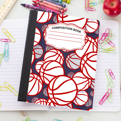 A composition notebook with a basketball pattern cover, placed on a lined notebook page surrounded by colorful paperclips, crayons, a ruler, and an apple.