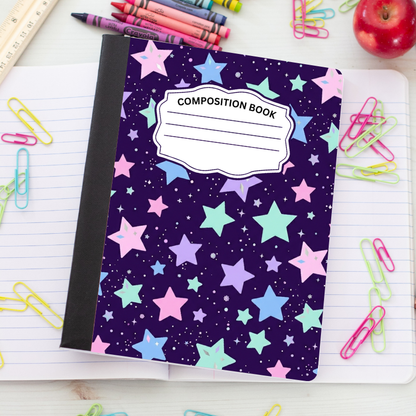 A composition book with a dark purple starry space cover pattern, placed on an open lined notebook surrounded by school supplies like colored paperclips, crayons, a ruler, and an apple.