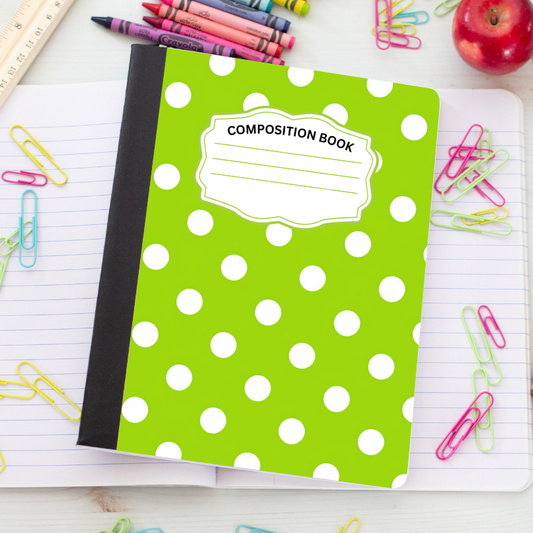 A green composition notebook with white polka dots and a black spine, placed on an open lined notebook surrounded by school supplies including crayons, paper clips, a ruler, and an apple.