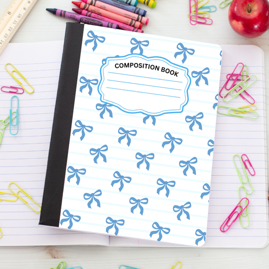 A composition book with a white cover, light blue horizontal stripes, and a repeating blue bow pattern, placed on an open lined notebook surrounded by school supplies like crayons, paperclips, a ruler, and an apple.