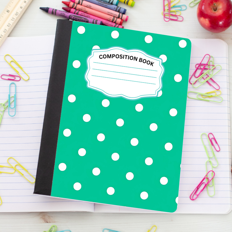 A green composition book with white polka dots and a blank label reading 'COMPOSITION BOOK' on the cover, placed on an open lined notebook surrounded by school supplies like paper clips, crayons, a ruler, and an apple.