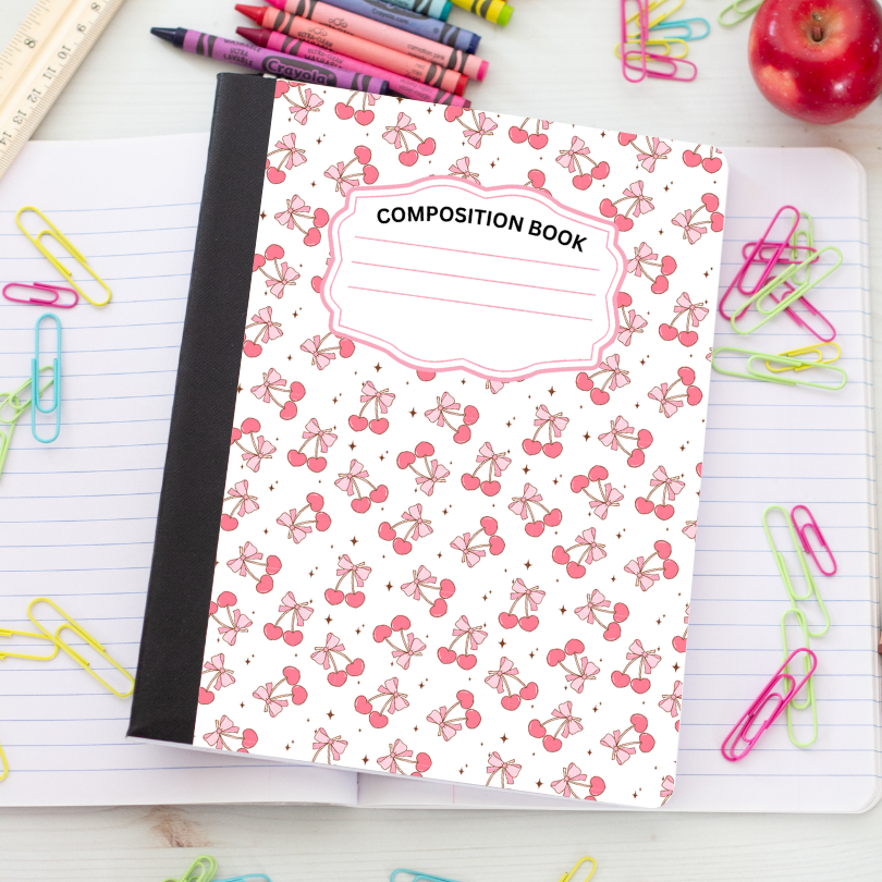 A composition notebook with a white cover decorated with a pink cherry and bow pattern, a black spine, and a label reading 'COMPOSITION BOOK'. It is styled on an open lined notebook surrounded by school supplies like paper clips, crayons, and an apple.
