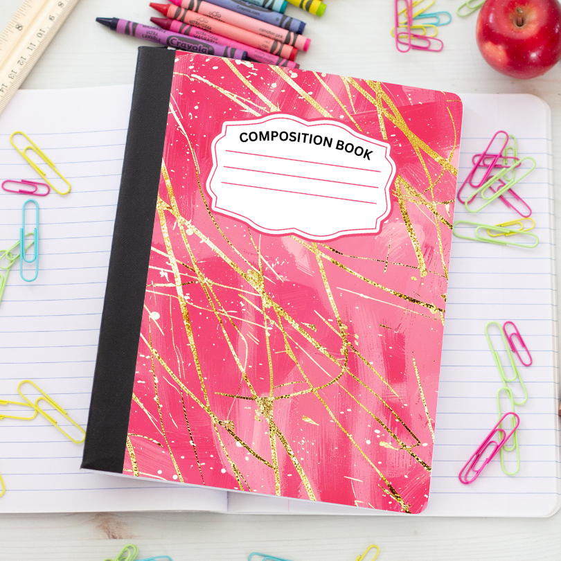 A pink composition notebook with a black spine and gold glitter-style diagonal lines, placed on an open lined notebook surrounded by school supplies including paper clips, crayons, a ruler, and an apple.