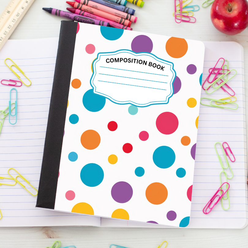 A composition book with a white cover decorated with colorful polka dots in blue, orange, purple, pink, yellow, and red, placed on an open lined notebook surrounded by school supplies like paperclips, crayons, and an apple.