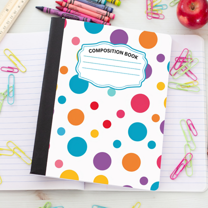 A composition book with a white cover decorated with colorful polka dots in blue, orange, purple, pink, yellow, and red, placed on an open lined notebook surrounded by school supplies like paperclips, crayons, and an apple.