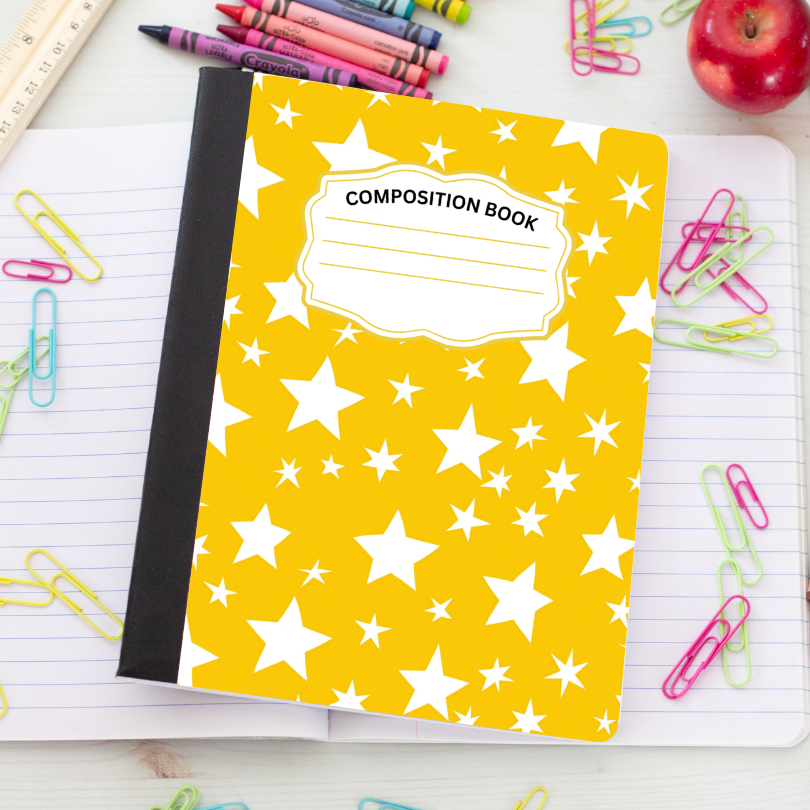 A yellow composition book with a white star pattern and a black spine, placed on an open lined notebook surrounded by school supplies including paper clips, crayons, a ruler, and an apple.